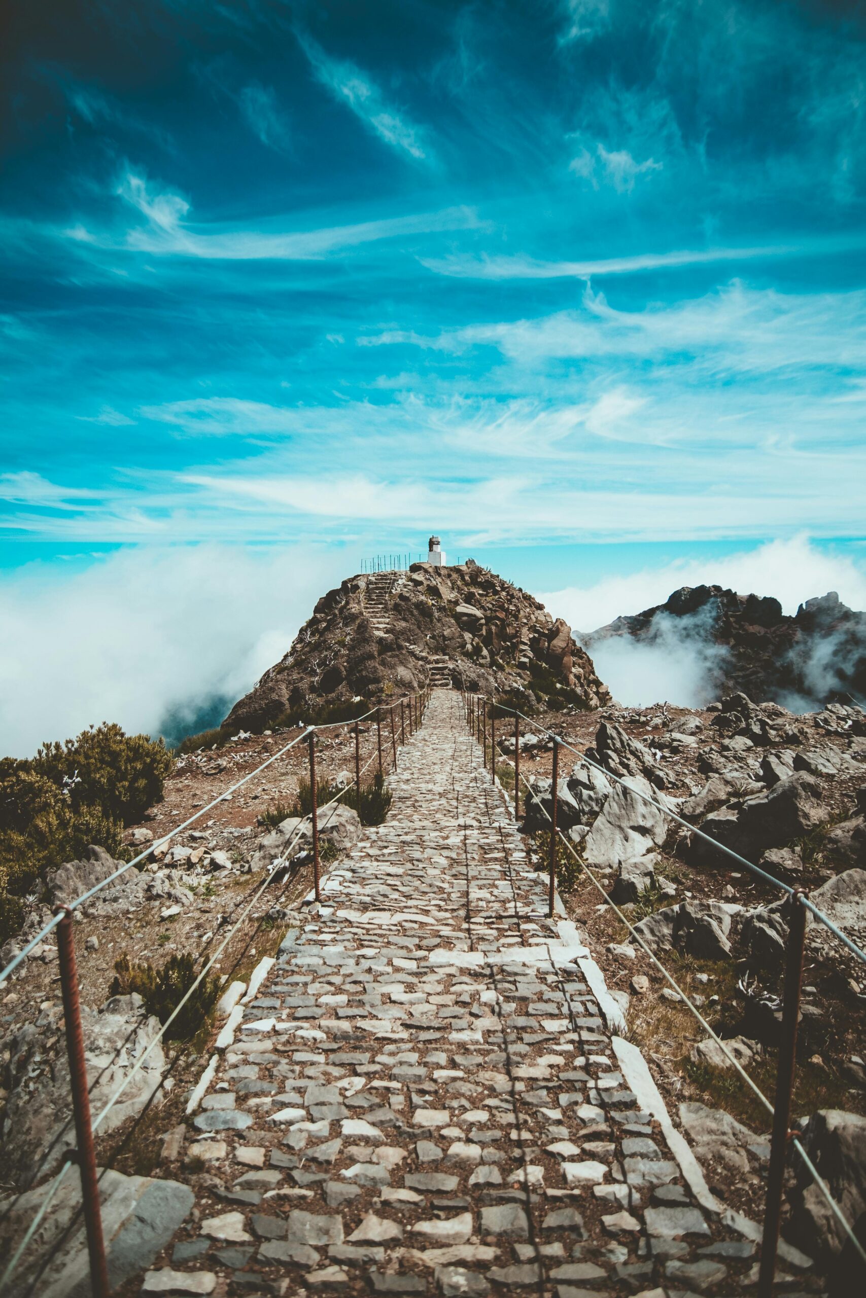 Stone path leading up to Pico do Arieiro summit in Madeira, under clear blue skies with distant clouds.